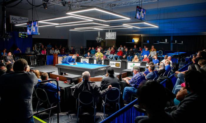 The International Open pool tournament under the lights, with tiers of spectators surrounding the table